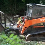 Orange Kubota SS1030 skid steer loader equipped with stump grinder attachment working in forested area for tree service operations